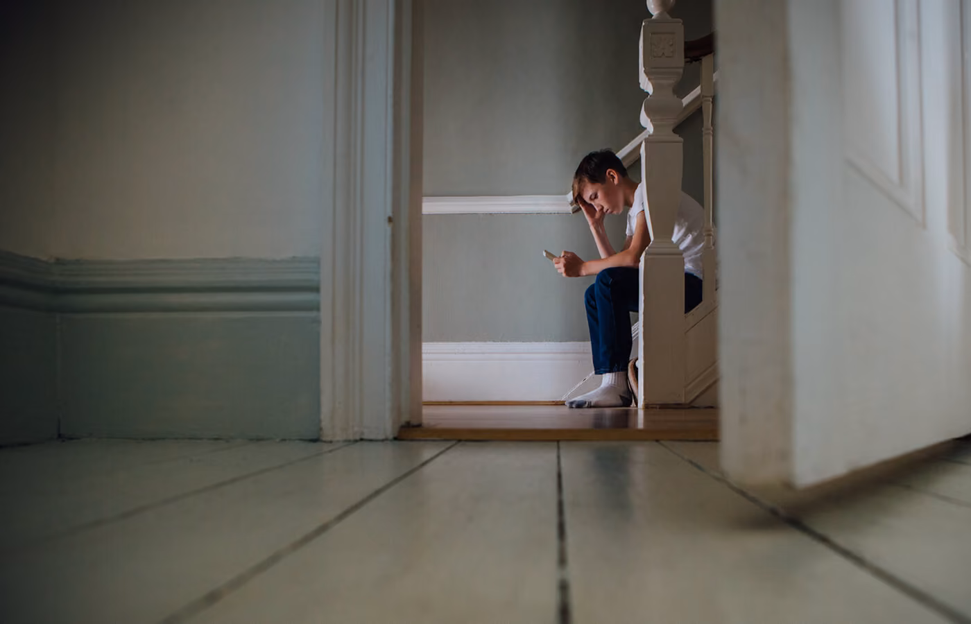 Boy sitting on stares sad and looking at mobile phone.